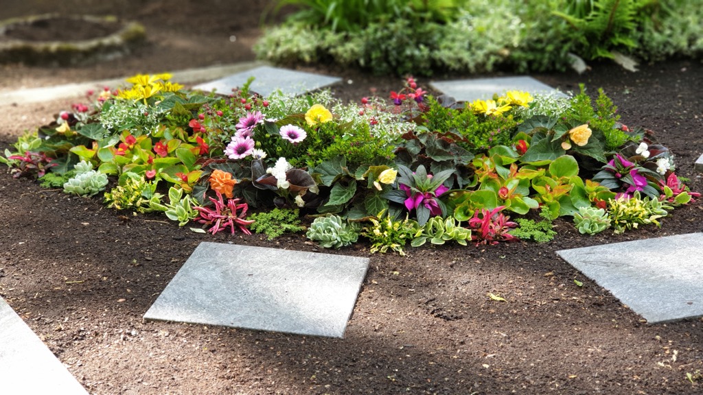 Rundes Beet mit vielen Blütenfarben in Gelb, Pink, Violett und Rot, Trittplatten ringsum