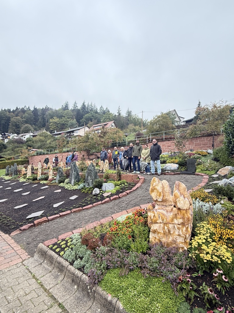 Gruppe von Gästen und Projektbeteiligten am neu gestalteten Erinnerungsgarten in Unterreichenbach, mit Natursteinstelen, einer Steinskulptur und einer Sandsteinmauer