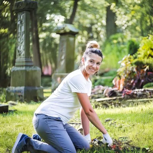 Mitarbeiterin bepflanzt kniend ein Grab zwischen alten Grabsteinen