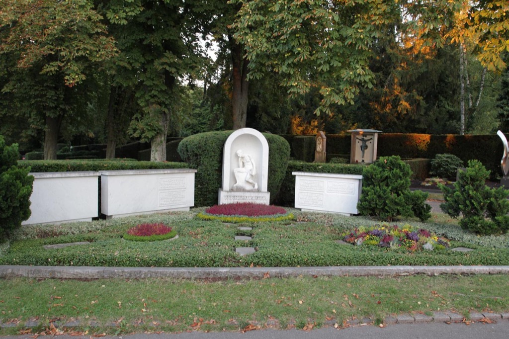 Familiengrab mit weißer Nischenstele, drei liegende weiße Grabplatten, herbstlich verfärbte Bäume