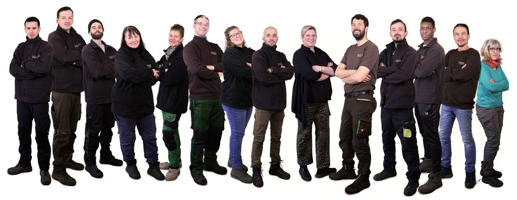 Gruppenfoto des Hilligardt-Teams: 14 Personen nebeneinander, die meisten in dunkler Arbeitskleidung und mit verschränkten Armen, freigestellt vor weißem Hintergrund