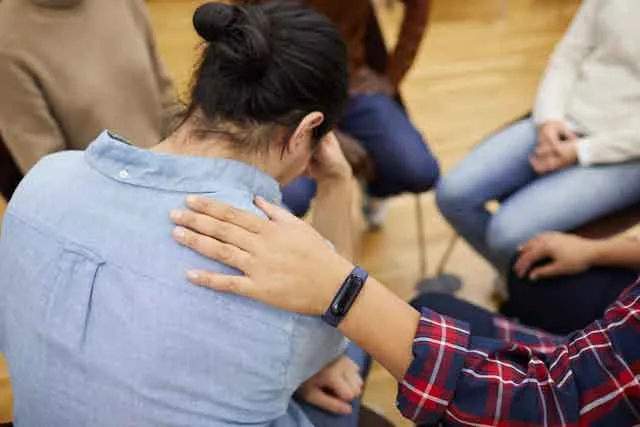 Tröstende Hand auf der Schulter einer sitzenden Person in einer Trauergruppe