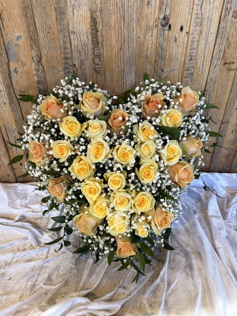 Herzförmiges Gesteck aus apricotfarbenen Rosen und Schleierkraut auf weißem Tuch